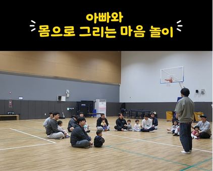 체육관에서 아빠와 아이들이 둘러앉아 수업을 듣는 모습